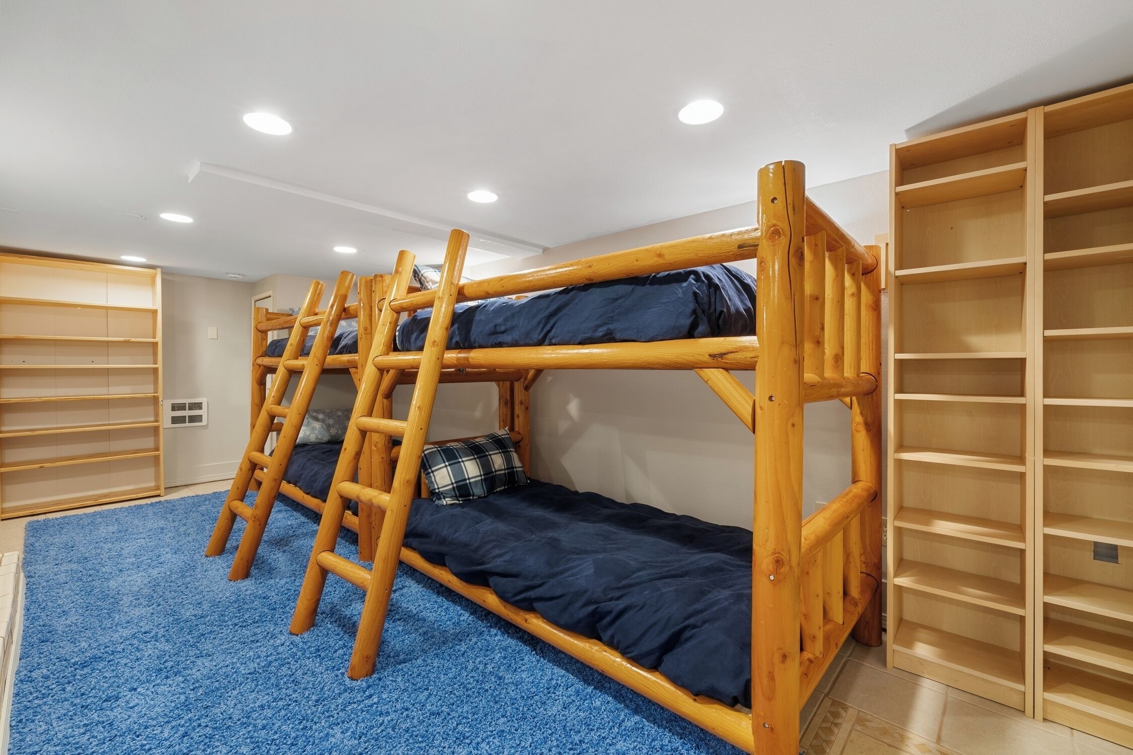A bunk bed room with a blue carpet, wooden bunk beds, and built-in shelving.