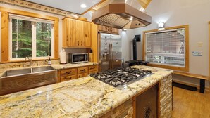 Una cocina con encimeras de granito, armarios de madera, electrodomésticos de acero inoxidable y un ventanal con persianas.