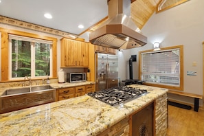Una cocina con encimeras de granito, armarios de madera, electrodomésticos de acero inoxidable y un ventanal con persianas.