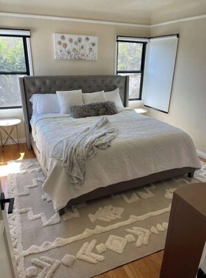 Relax in this serene bedroom with a large bed and tufted headboard, featuring a window and a convenient whiteboard.