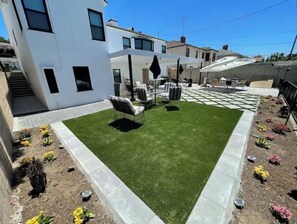 Uma casa moderna com um gramado bem cuidado, móveis de jardim e diversas plantas.