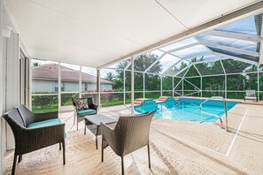 Un espacio al aire libre cubierto con piscina, mobiliario de mimbre y vistas del barrio circundante.