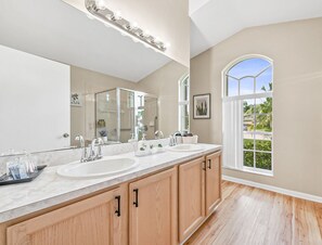 Un baño con un espejo grande, dos lavabos, armarios de madera y vistas al exterior por una ventana.