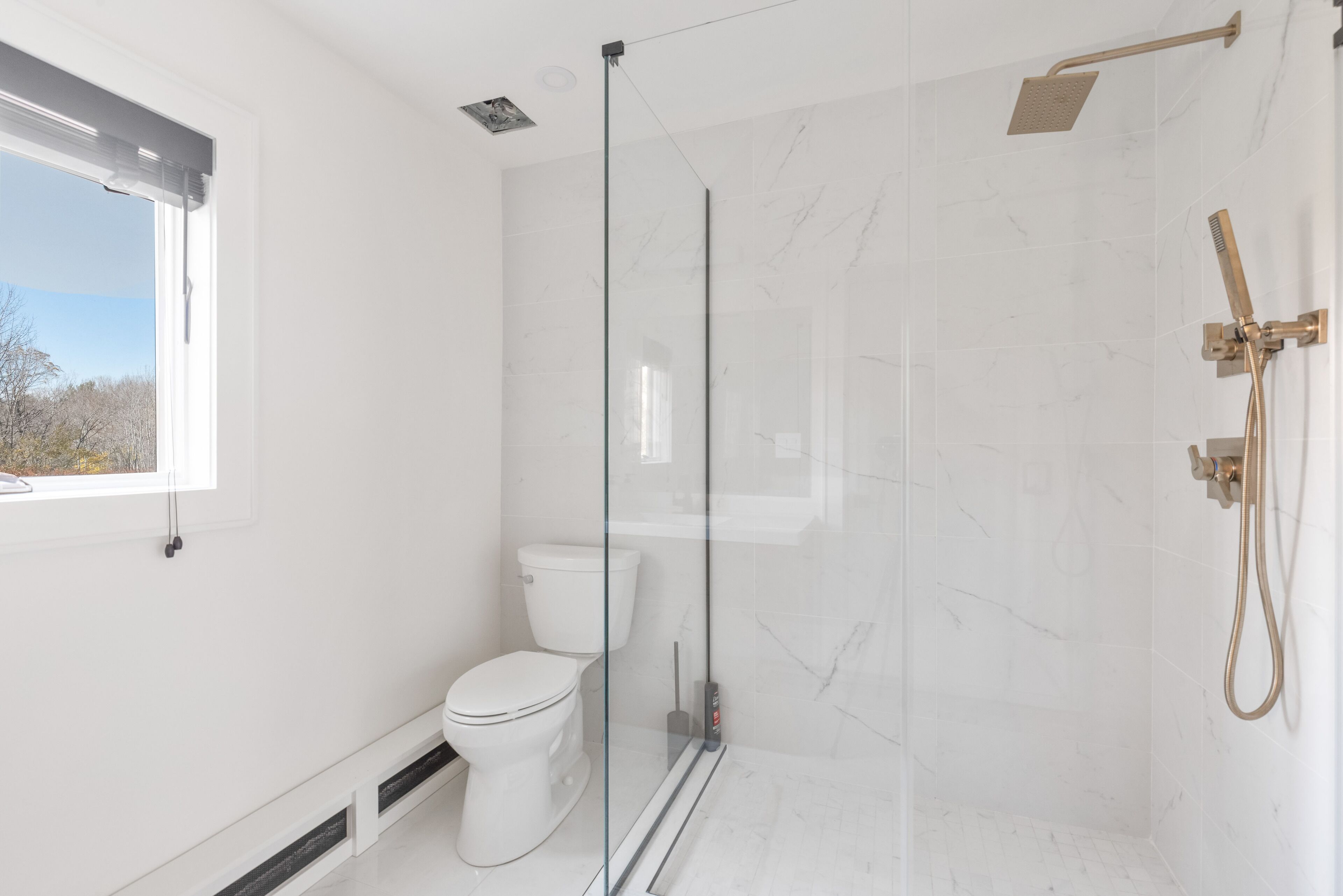 Un baño moderno con ducha de vidrio, inodoro y ventana que proporciona luz natural.