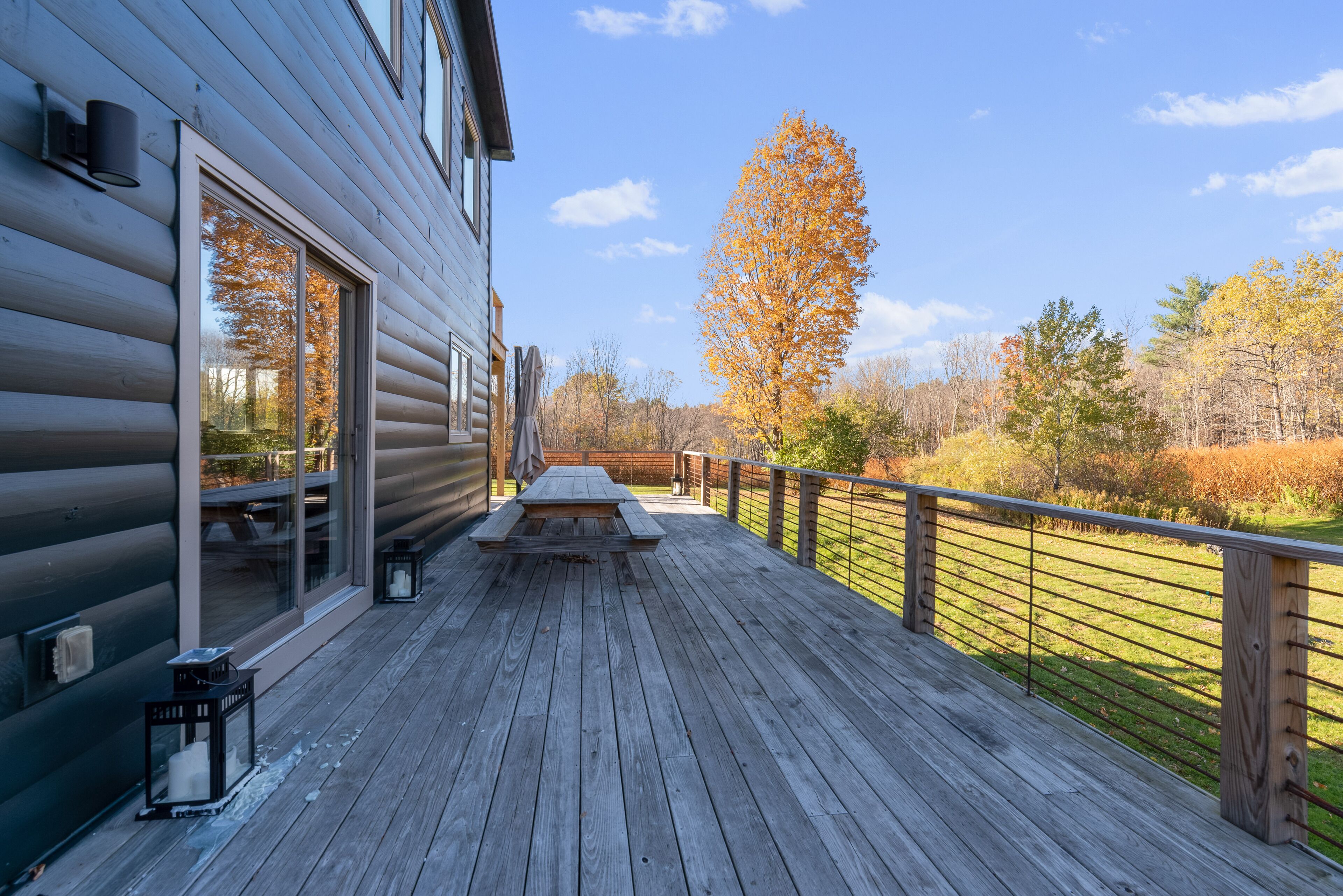 A wooden deck with a picnic table and benches, overlooking a grassy area with trees.