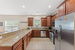 A kitchen with granite countertops, wooden cabinets, stainless steel appliances, and a window with blinds. - 5BR | Sleeps 17 | Pool | Close To The Beach | 7092 (North Myrtle Beach)