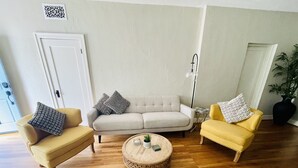 Ett vardagsrum med en beige soffa, en gul fåtölj och ett runt soffbord.