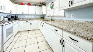 A kitchen with white cabinets, a granite countertop, and a tiled floor. - 6BR | Sleeps 16 | Pool | Steps To The Beach |20427 (North Myrtle Beach)