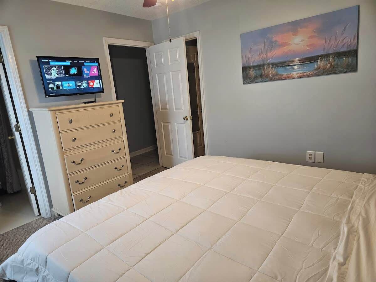 Een slaapkamer met een bed, een dressoir, een televisie en een schilderij aan de muur.
