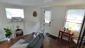 A cozy living room with a gray sofa, a fireplace, and a dining area with a table and chairs. - Romantic Tiny Cabin- With Lake View (Lake Arrowhead)