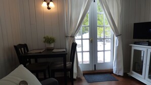 A cozy room with a wooden floor, a dining table with chairs, a television on a cabinet, and a window with curtains. - Romantic Tiny Cabin- With Lake View (Lake Arrowhead)