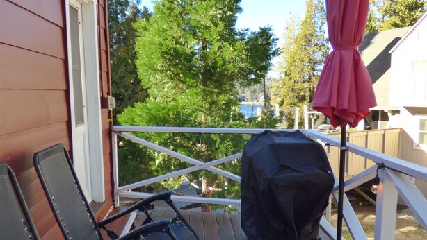 A wooden deck with a grill and chairs, overlooking a backyard with trees and a house. - Romantic Tiny Cabin- With Lake View (Lake Arrowhead)