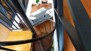 A spiral staircase with a wooden floor landing area, a sofa, and a small table with a plant. - Romantic Tiny Cabin- With Lake View (Lake Arrowhead)