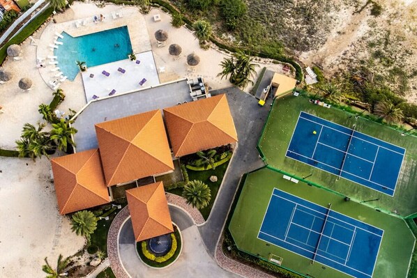 An aerial view of a resort with a swimming pool, tennis courts, and a circular fountain.