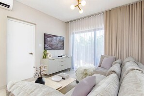 A modern living room with a sofa, a coffee table, a TV, and a window with curtains.