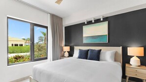 A modern hotel room with a large bed, two bedside tables, a window with a view of greenery and a building, and a painting on the wall.