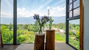 A room with a large window offering a view of a mountainous landscape and a transmission tower. - Dali Village Inn (Dali City)