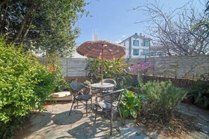 An outdoor patio with a table and chairs, surrounded by plants and a fence.