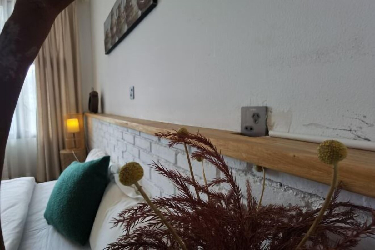 A hotel room with a white bed, teal pillow, and a wooden headboard.