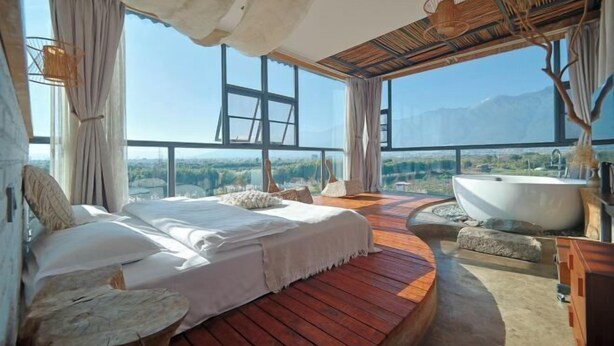 A bedroom with a large bed, a wooden floor, a bathtub, and a view of the mountains. - Dali Village Inn (Dali City)