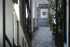 A narrow corridor with tiled flooring, potted plants, and a wall-mounted target. - Dali Village Inn (Dali City)