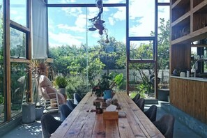 A wooden dining table with chairs, surrounded by large windows and potted plants. - Dali Village Inn (Dali City)