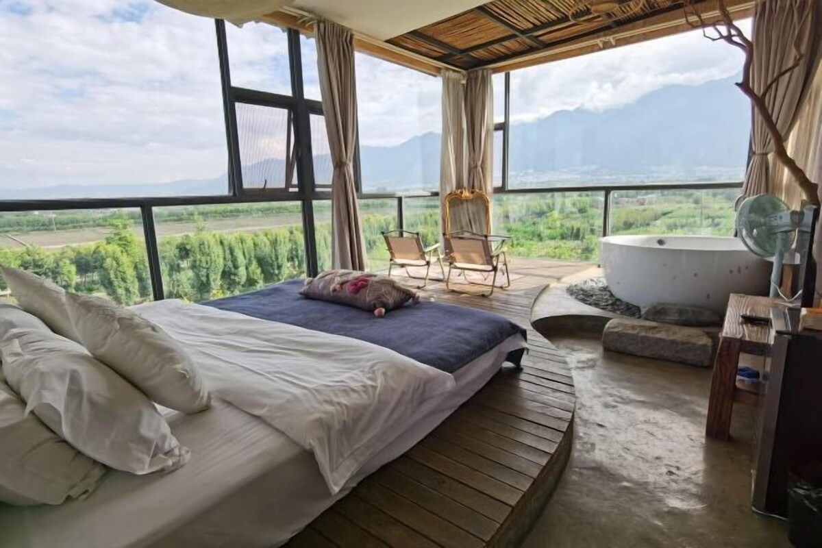 A bedroom with a large bed, a view of mountains, and a hot tub.