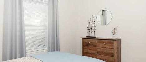 A bedroom with a bed, a dresser, a mirror, and a window with curtains.