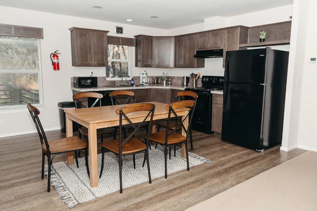 Una cocina moderna con armarios de madera, un refrigerador negro y una mesa de comedor con sillas.