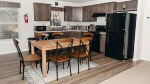 A modern kitchen with wooden cabinets, a black refrigerator, and a dining table with chairs. - Neptune Haven Getaway Near the Ocean  (Ferndale)