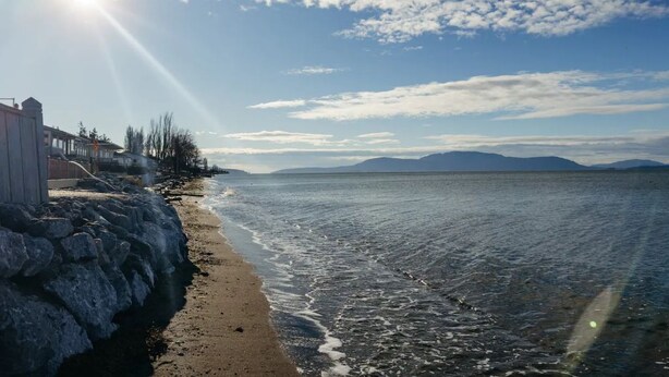 A beach with a stone wall, a row of buildings, and a clear sky. - Neptune Haven Getaway Near the Ocean  (Ferndale)