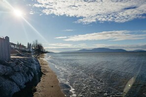 A beach with a stone wall, a row of buildings, and a clear sky. - Neptune Haven Getaway Near the Ocean (Ferndale)