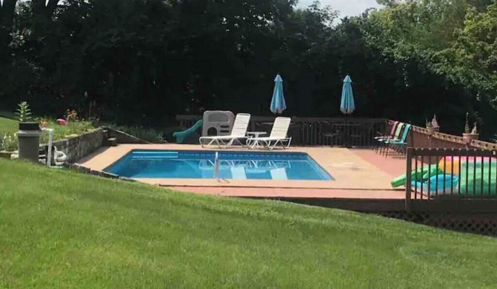 A rectangular swimming pool with a tiled deck, surrounded by a grassy area.