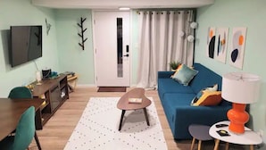 A living room with a blue sofa, a small table, a TV, and a door leading to another room. - Mod Lodge
Pool open until Sept 20th
Pets Welcome 
EV charging (Edgewood)