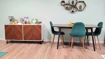 A dining area with a wooden cabinet, teal chairs, and a hexagonal wall decoration.