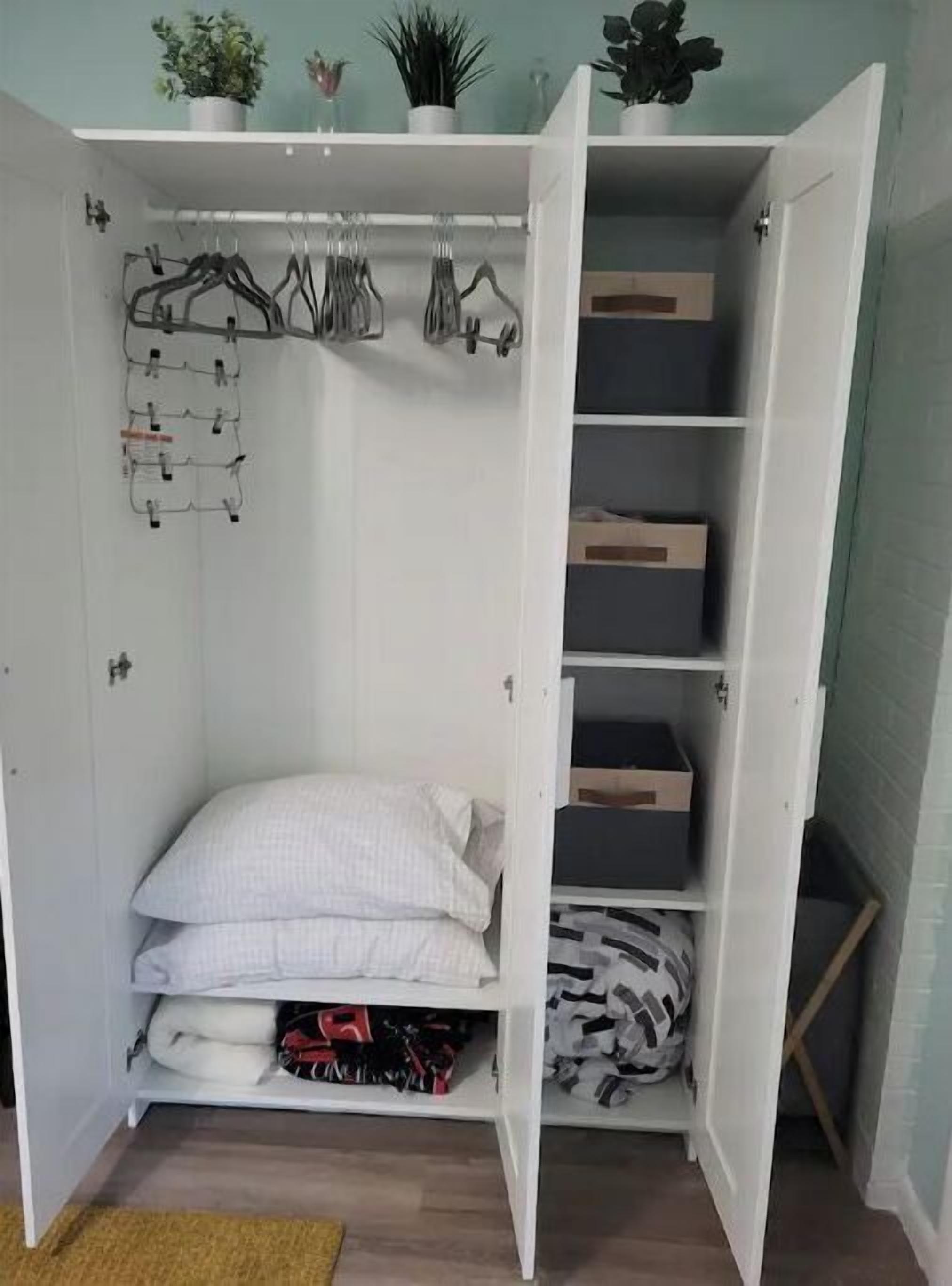Une armoire blanche dotée de nombreuses étagères et d’un espace pour suspendre les vêtements, contenant des vêtements pliés et des cintres.