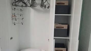 Une armoire blanche dotée de nombreuses étagères et d’un espace pour suspendre les vêtements, contenant des vêtements pliés et des cintres.
