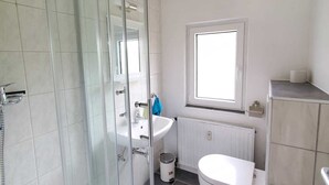 A modern bathroom with a glass shower enclosure, a white sink, and a toilet. - Sch(l)afgemach Schäferwagen - Farm in the Eifel (Nettersheim)