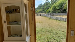 A wooden interior with a white cabinet, a door leading outside, and a view of a fenced yard. - Sch(l)afgemach Schäferwagen - Farm in the Eifel (Nettersheim)