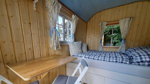 A cozy cabin room with a wooden interior, a bed with checkered bedding, a small table, and two chairs. - Sch(l)afgemach Schäferwagen - Farm in the Eifel (Nettersheim)