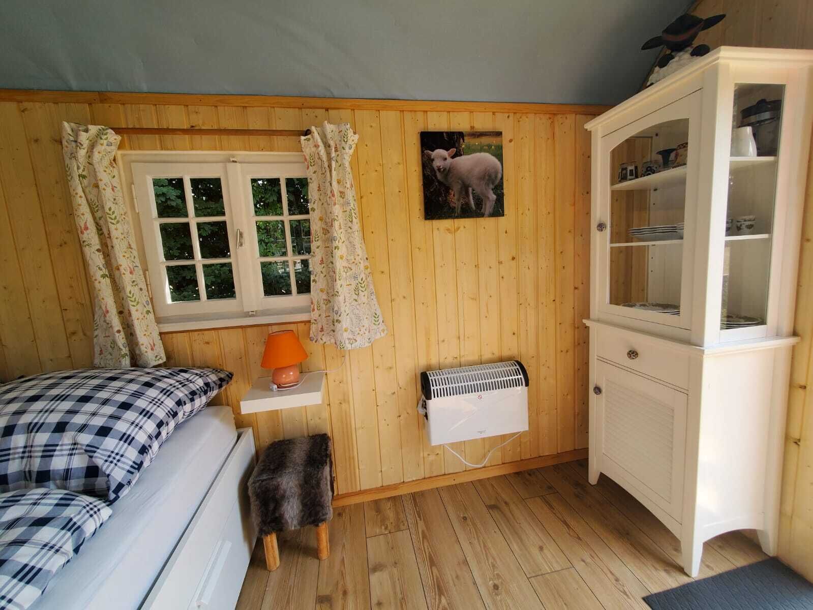 Kodikas huone, jossa on sänky, pieni pöytä lampun kanssa, patteri ja kaappi.
