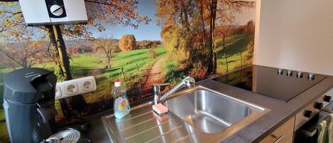 A kitchen with a stainless steel sink, a coffee maker, and a kettle.