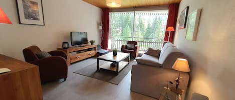 A modern living room with a wooden ceiling, a flat-screen TV, a sofa, a coffee table, and a dining table.