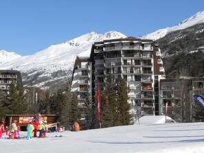 Ein mehrstöckiges Hotel mit Balkonen vor einer verschneiten Bergkulisse.