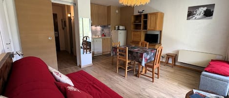 A compact living space with a kitchenette, a dining area, and a bedroom with a red sofa.