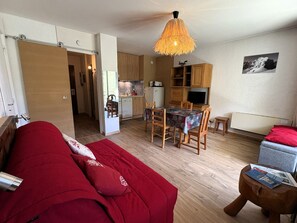 Ein kompakter Wohnraum mit Küchenzeile, Essbereich und Schlafzimmer mit rotem Sofa.