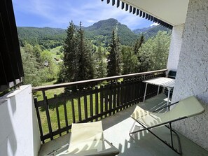 Ein Balkon mit Blick auf ein bewaldetes Gebirge, einem Tisch und einem Stuhl.