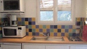 Una cocina con armarios blancos, un lavamanos de acero inoxidable y una ventana sobre el lavamanos.