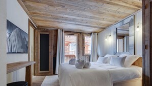 A bedroom with a wooden ceiling, a bed with white bedding, a small desk, and a large mirror. - Charming apartment for 8 with parking and WIFI near the slopes (Montvalezan-La Rosière)