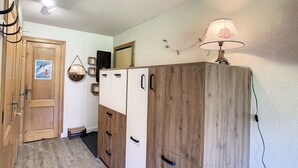 A room with a wooden wardrobe, a door with a 'Mont Blanc' sticker, a small table with a lamp, and a mirror on the wall. - Charming 2-room apt in Combloux with terrace, parking and ski locker (Combloux)
